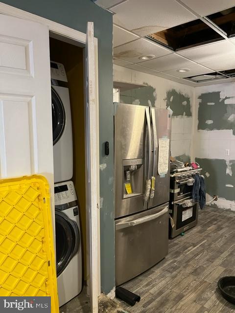 kitchen featuring a paneled ceiling, stainless steel fridge with ice dispenser, stacked washer and clothes dryer, and dark hardwood / wood-style flooring