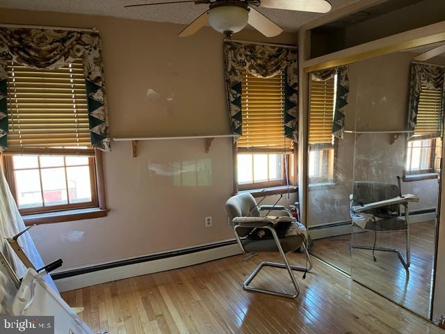 sitting room featuring ceiling fan, a baseboard heating unit, light hardwood / wood-style flooring, and a healthy amount of sunlight