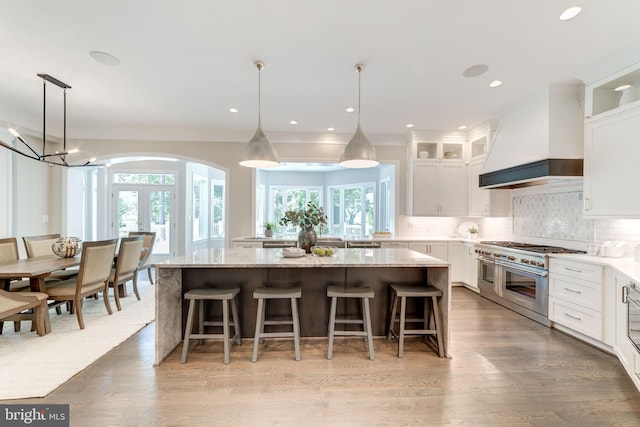 kitchen with white cabinetry, custom range hood, range with two ovens, and a kitchen island with sink