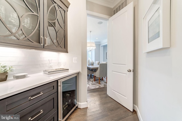 bar featuring beverage cooler, backsplash, ornamental molding, and dark wood-type flooring