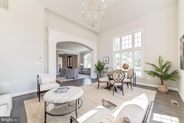 living room featuring a towering ceiling, a healthy amount of sunlight, a chandelier, and dark hardwood / wood-style flooring