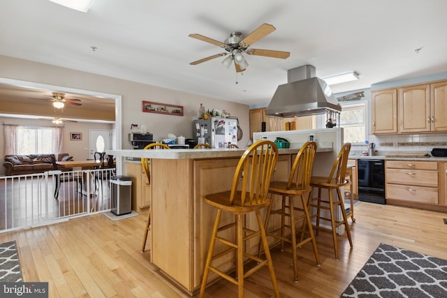 kitchen with a kitchen bar, ceiling fan, island range hood, and light wood-type flooring