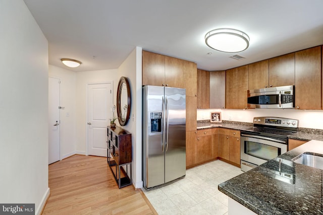 kitchen with appliances with stainless steel finishes, light tile floors, and dark stone countertops