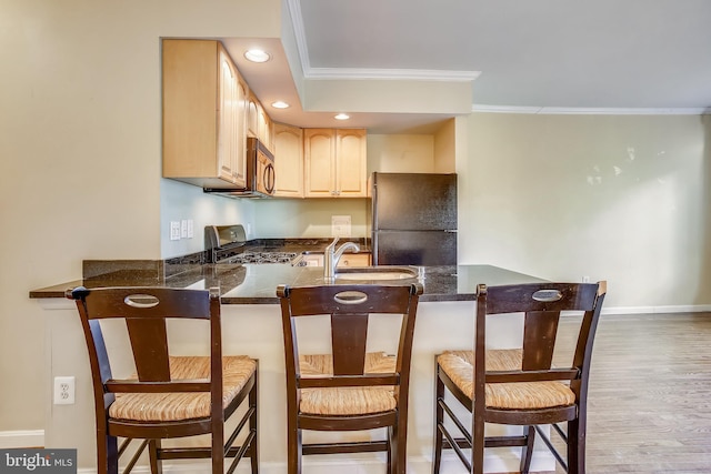 kitchen featuring kitchen peninsula, light hardwood / wood-style floors, black refrigerator, and a kitchen breakfast bar