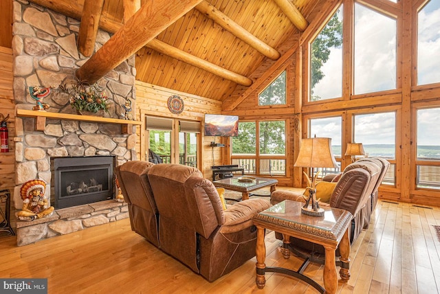 living room with light hardwood / wood-style floors, a stone fireplace, beam ceiling, wood ceiling, and high vaulted ceiling