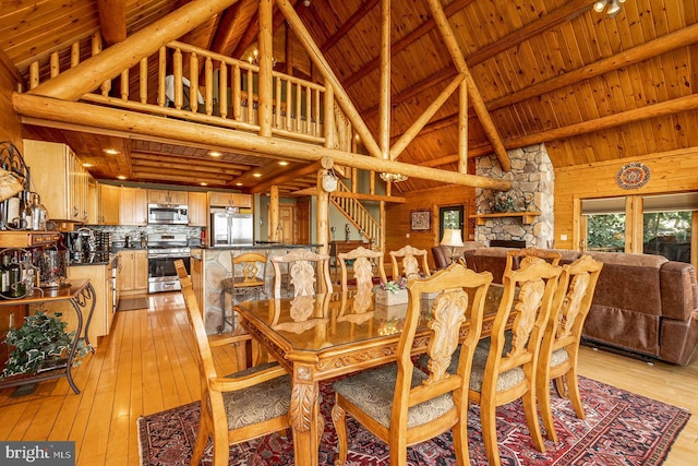 dining area with a fireplace, light hardwood / wood-style flooring, beam ceiling, high vaulted ceiling, and wood ceiling