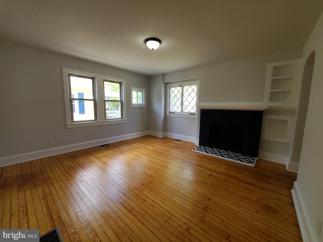 unfurnished living room featuring built in shelves, a brick fireplace, and light wood-type flooring