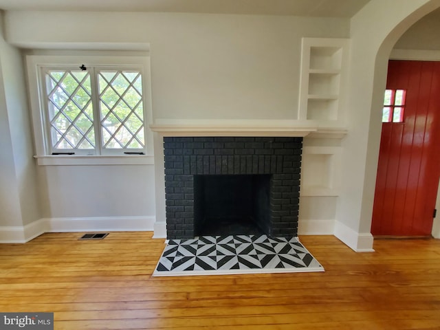 unfurnished living room with built in features, a fireplace, light hardwood / wood-style floors, and a healthy amount of sunlight