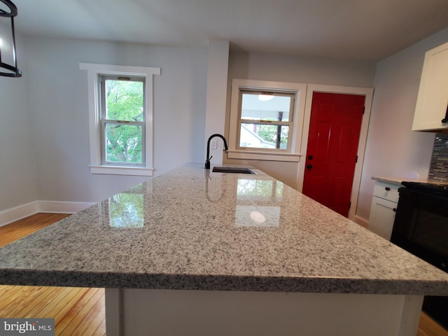 kitchen with sink, light stone counters, light hardwood / wood-style flooring, a center island with sink, and white cabinetry