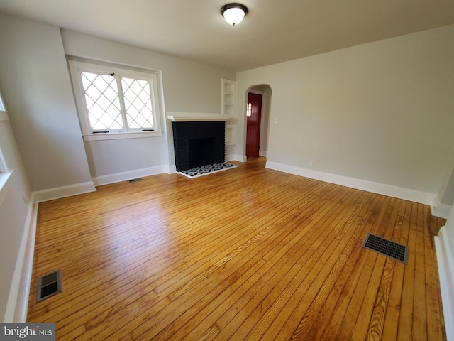 unfurnished living room with light wood-type flooring and a brick fireplace