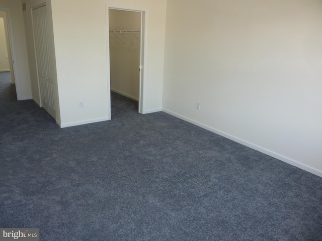 unfurnished bedroom with a closet, dark carpet, and a walk in closet