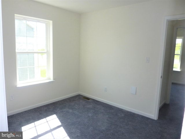 empty room featuring dark carpet and plenty of natural light