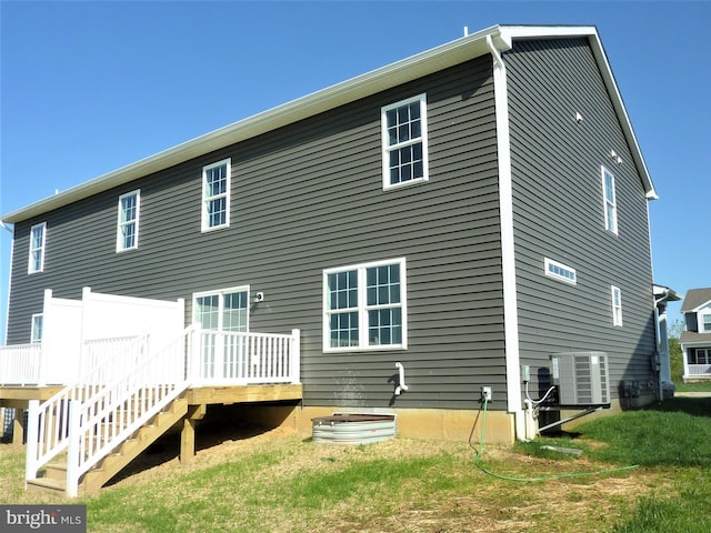 back of property with a deck, central air condition unit, and a yard