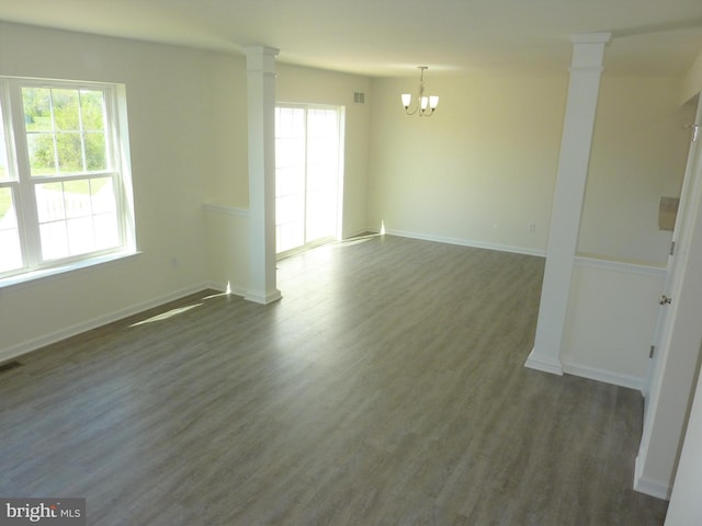 spare room with dark hardwood / wood-style flooring, an inviting chandelier, and decorative columns