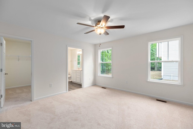 unfurnished bedroom with light colored carpet, a spacious closet, ceiling fan, a closet, and connected bathroom