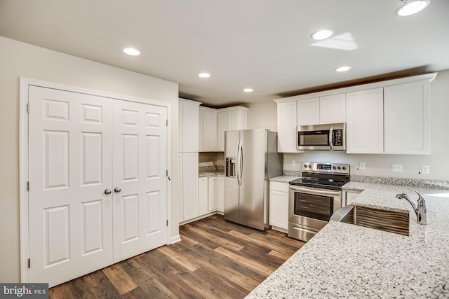 kitchen with stainless steel appliances, dark hardwood / wood-style floors, light stone counters, white cabinets, and sink