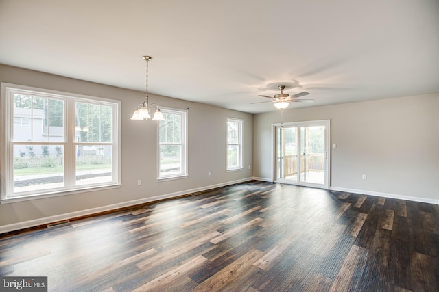 empty room featuring dark hardwood / wood-style flooring, ceiling fan with notable chandelier, and a wealth of natural light