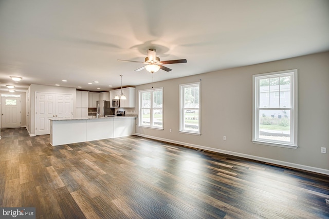 unfurnished living room with ceiling fan with notable chandelier and dark hardwood / wood-style floors