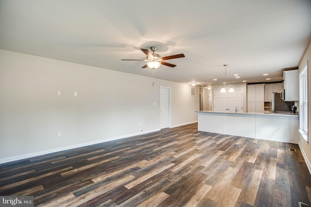 unfurnished living room with ceiling fan with notable chandelier and dark wood-type flooring