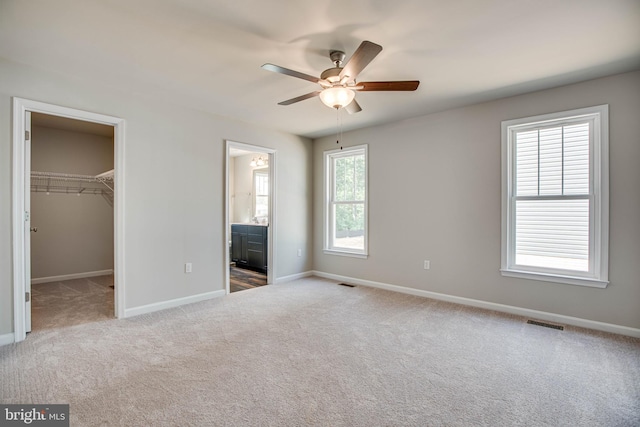 unfurnished bedroom featuring light carpet, a closet, ensuite bathroom, ceiling fan, and a walk in closet