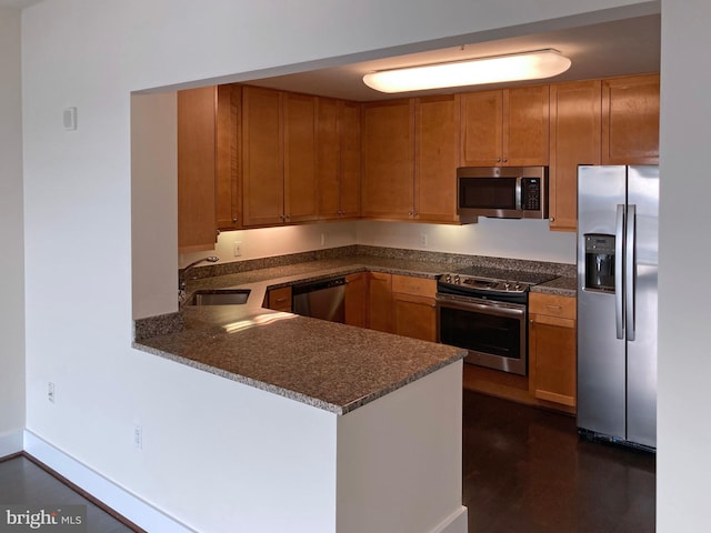 kitchen with brown cabinets, appliances with stainless steel finishes, a peninsula, and baseboards