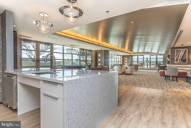 interior space with a tray ceiling, a sink, light wood-style floors, decorative light fixtures, and open floor plan