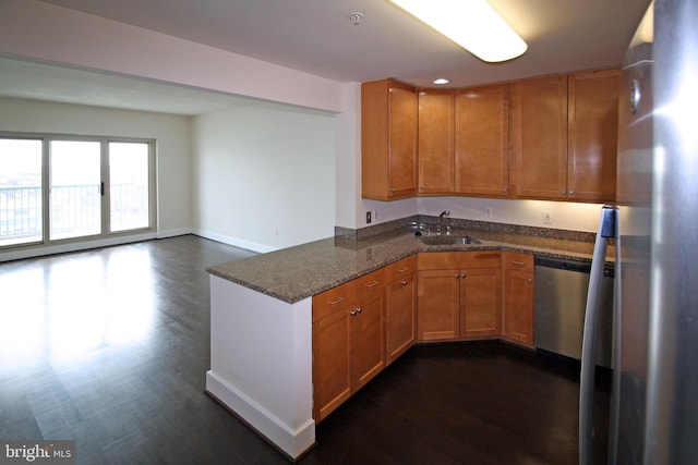 kitchen with dark stone counters, appliances with stainless steel finishes, a peninsula, dark wood-style floors, and a sink