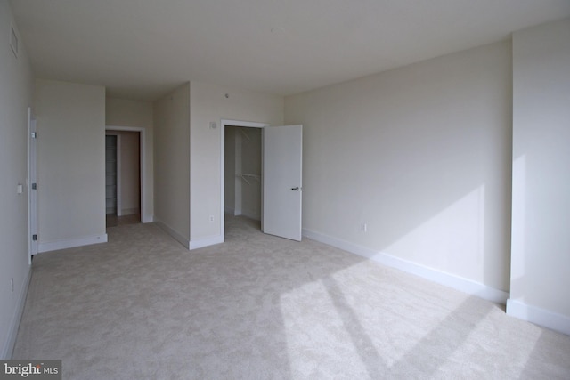 unfurnished bedroom with a spacious closet, baseboards, a closet, and light carpet