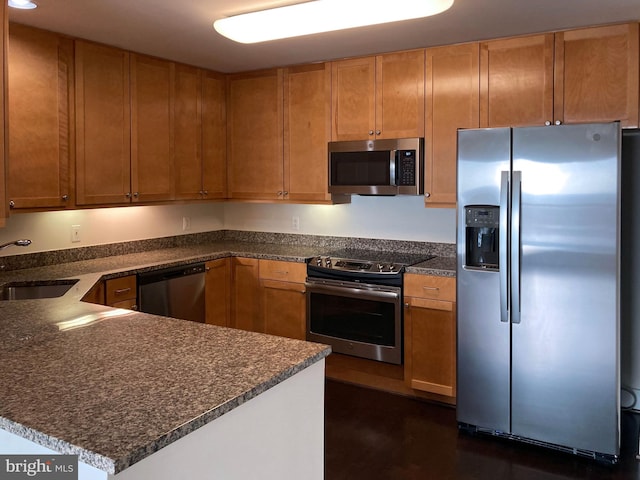 kitchen featuring brown cabinets, a peninsula, stainless steel appliances, and a sink