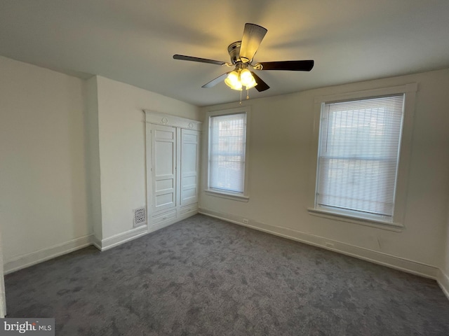 unfurnished bedroom featuring ceiling fan, dark carpet, and a closet