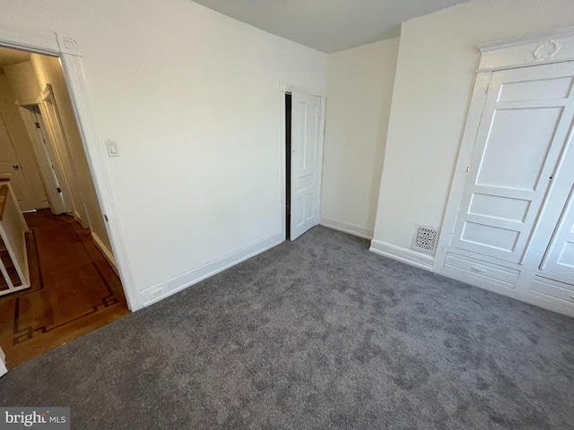 unfurnished bedroom with dark carpet and a closet