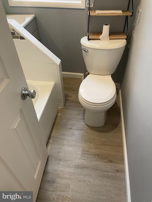 bathroom with toilet, hardwood / wood-style floors, and a tub