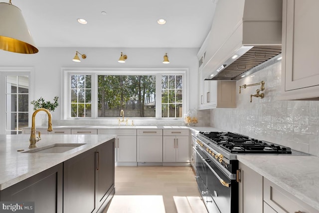 kitchen with custom range hood, light hardwood / wood-style flooring, high end stove, backsplash, and sink