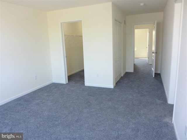 unfurnished bedroom with a closet, dark colored carpet, and a walk in closet