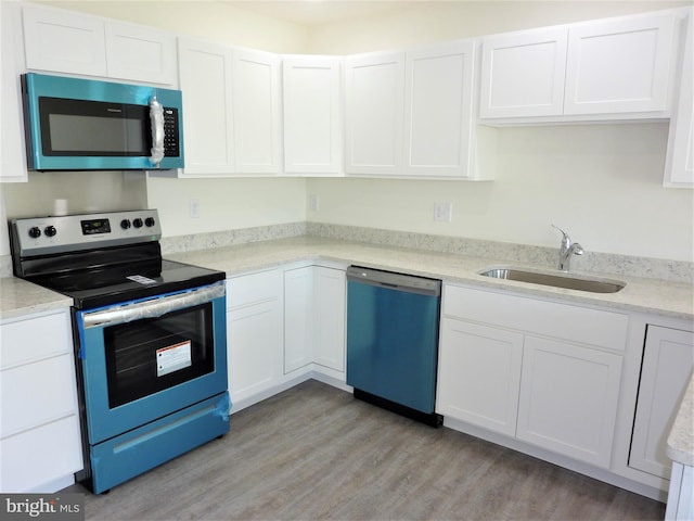 kitchen with appliances with stainless steel finishes, light hardwood / wood-style floors, sink, white cabinetry, and light stone countertops