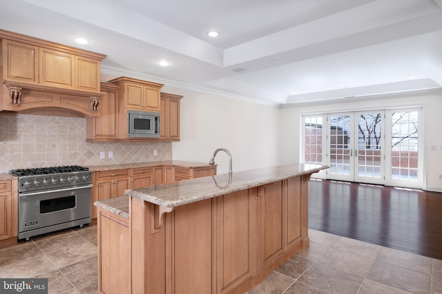 kitchen with stainless steel microwave, backsplash, a tray ceiling, light wood-type flooring, and gas range