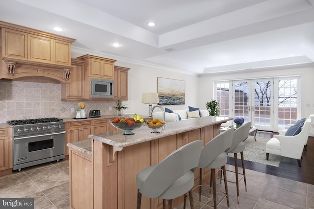 kitchen with range with gas cooktop, stainless steel microwave, a raised ceiling, and a breakfast bar area