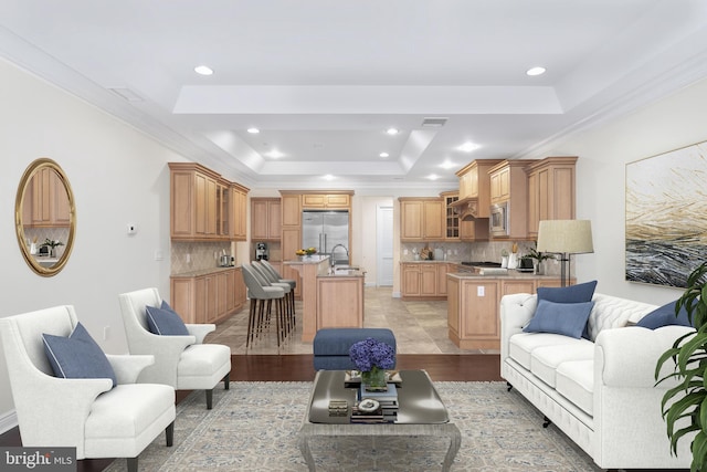 living room with sink, light hardwood / wood-style flooring, ornamental molding, and a raised ceiling