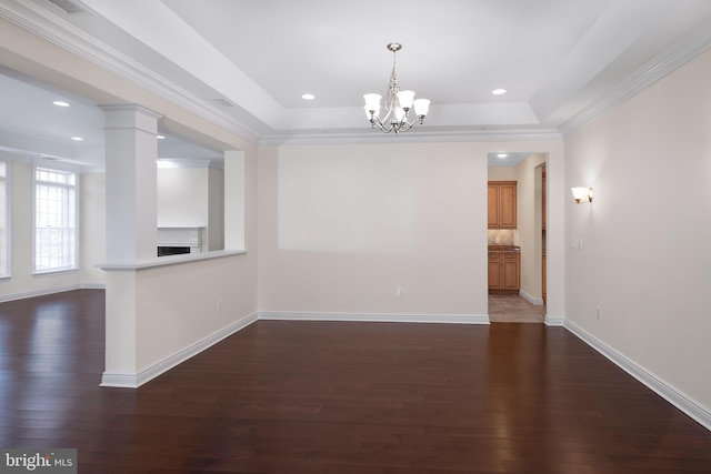 unfurnished room with dark hardwood / wood-style floors, a raised ceiling, ornamental molding, a chandelier, and decorative columns