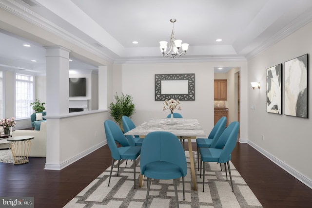 dining space with dark hardwood / wood-style floors, ornamental molding, decorative columns, a tray ceiling, and an inviting chandelier