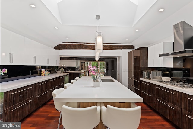 kitchen with a kitchen breakfast bar, dark wood-type flooring, wall chimney exhaust hood, and stainless steel gas cooktop