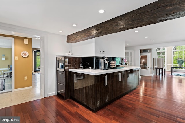 kitchen featuring beamed ceiling, backsplash, a kitchen bar, light hardwood / wood-style floors, and dark brown cabinetry