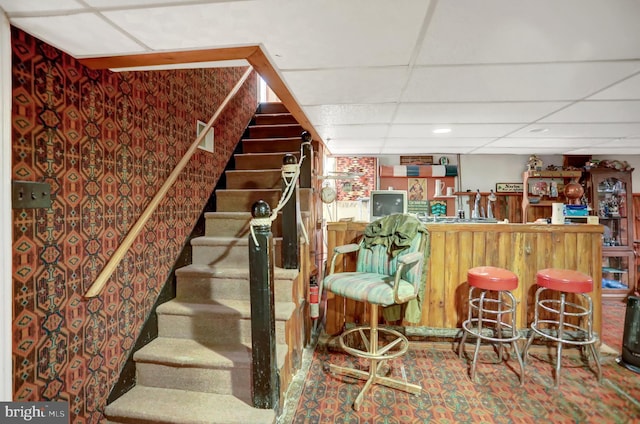 staircase featuring dark carpet, indoor bar, and a drop ceiling