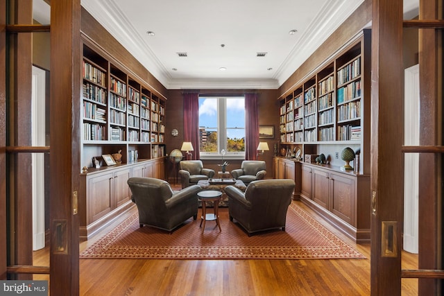 living area with ornamental molding, built in shelves, and light wood-type flooring