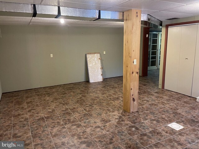 basement featuring a paneled ceiling and dark tile floors