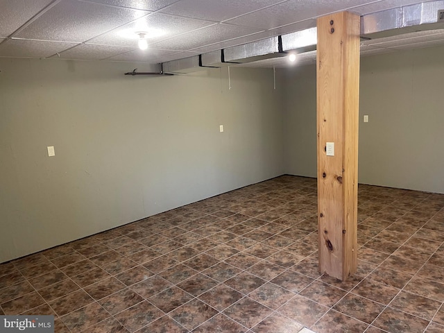 basement with a paneled ceiling and dark tile floors