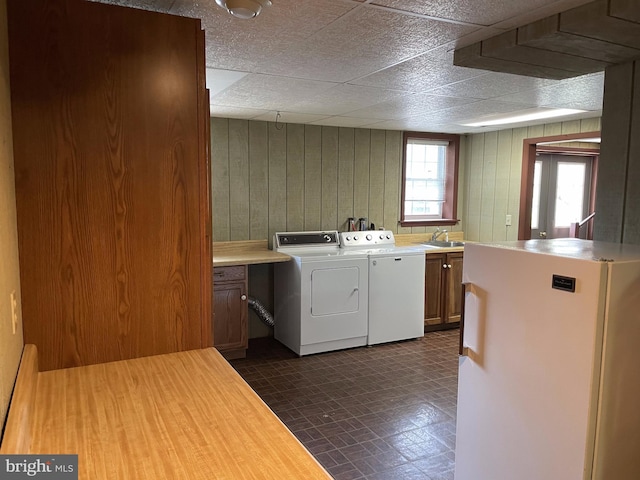 clothes washing area with cabinets, sink, separate washer and dryer, wooden walls, and dark tile flooring