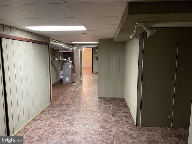 hall featuring a paneled ceiling and dark tile flooring