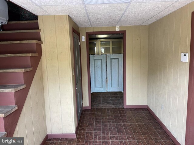 hall with wood walls and a drop ceiling