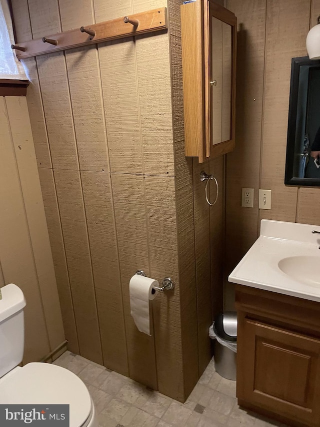 bathroom featuring wooden walls, toilet, tile floors, and vanity